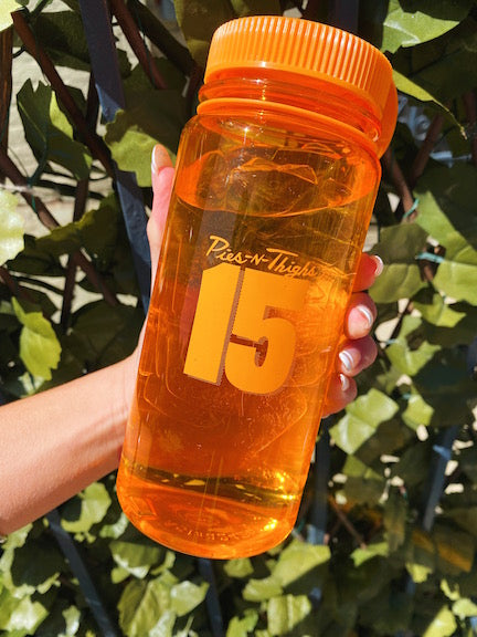 Pies n Thighs 15th anniversary clear orange water bottle against leafy background