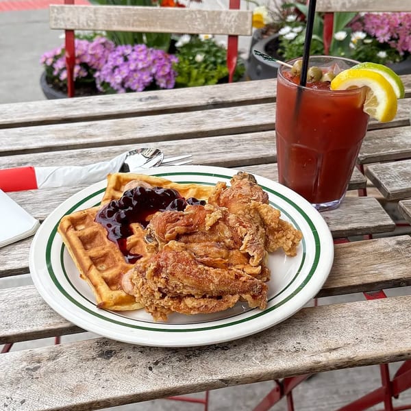 Pies 'n' Thighs fried chicken and waffles with blueberry compote, and a Bloody Mary on a wooden table.