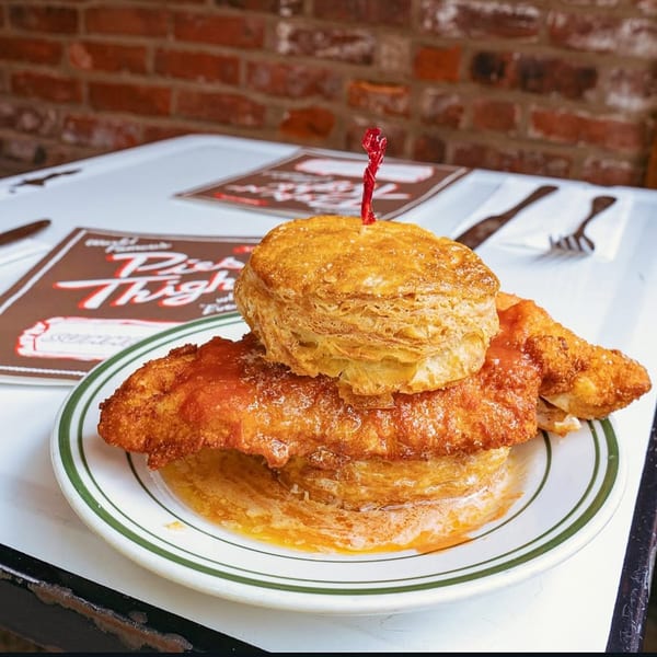 A fried chicken and biscuit sandwich with hot sauce and honey on a white plate.