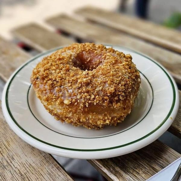 A Pies 'n' Thighs donut, covered in crunchy crumbs, sits on a white plate with a green rim.