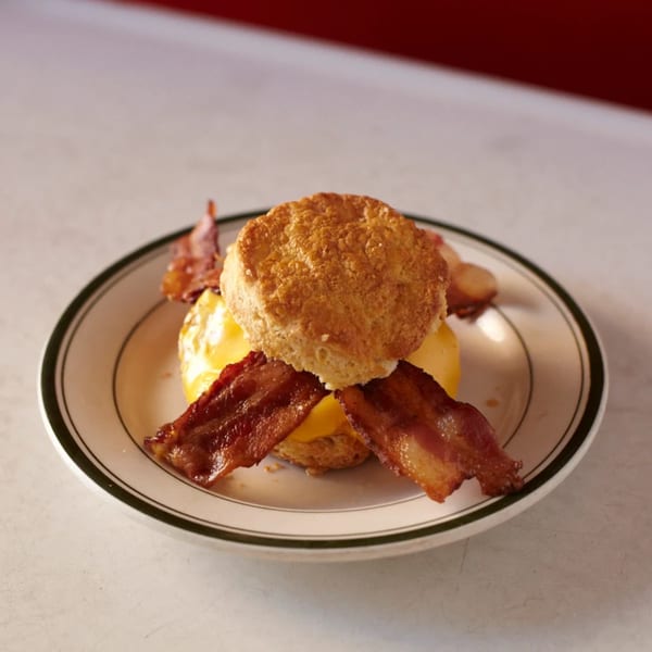 A golden biscuit sandwich with melted cheese and crispy bacon on a white plate with a green rim.