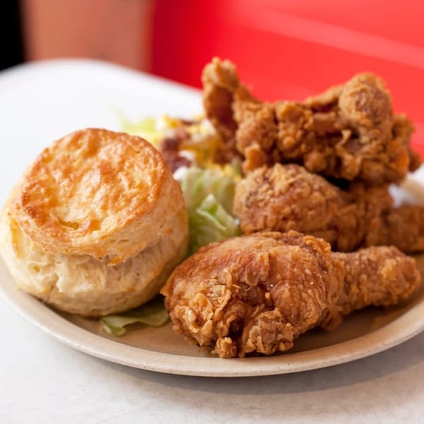 A plate of golden-brown fried chicken pieces and a fluffy biscuit from Pies 'n' Thighs.