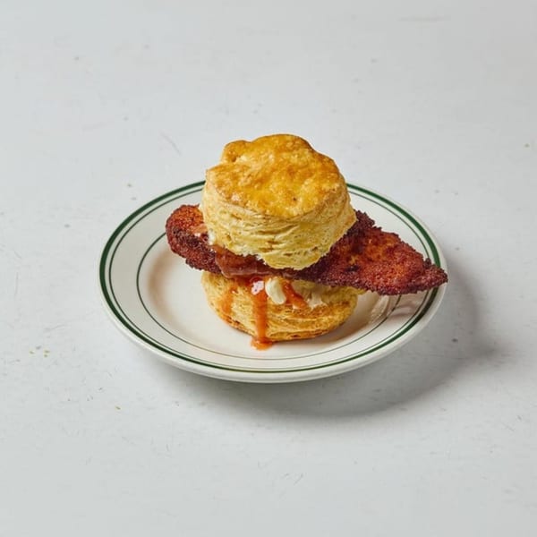 Pies 'n' Thighs' fried chicken biscuit with hot sauce and butter on a white plate.