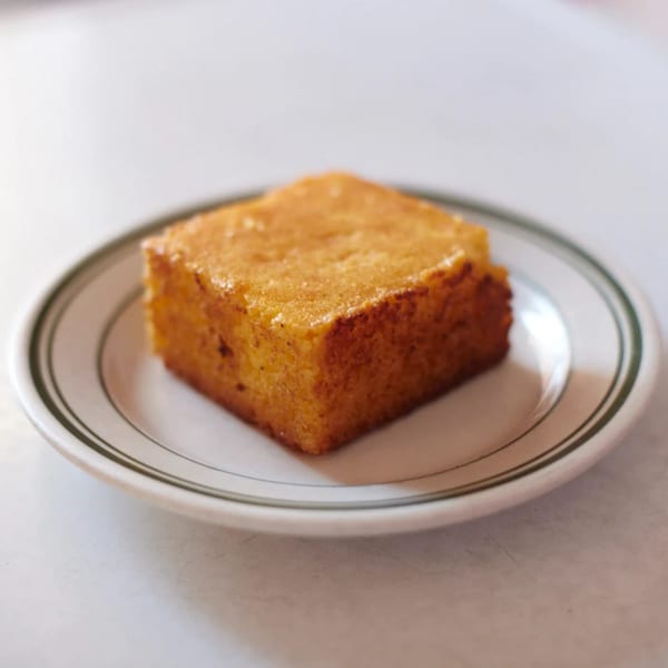 A golden-brown square of cornbread sits on a white plate with a green rim.